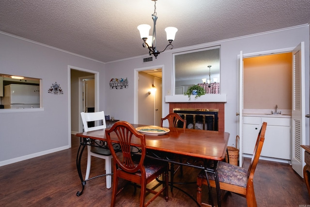 dining space featuring dark hardwood / wood-style flooring, crown molding, a chandelier, a textured ceiling, and a tiled fireplace