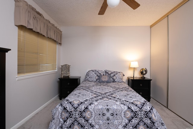 bedroom with ceiling fan, light colored carpet, a textured ceiling, and a closet