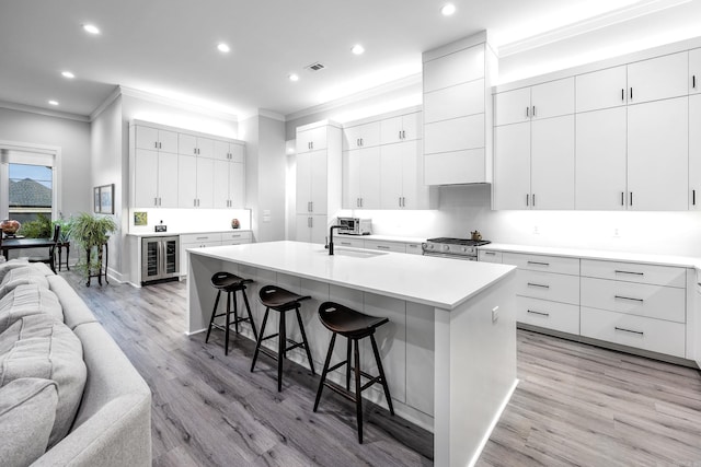 kitchen with a kitchen breakfast bar, white cabinets, an island with sink, and light hardwood / wood-style floors