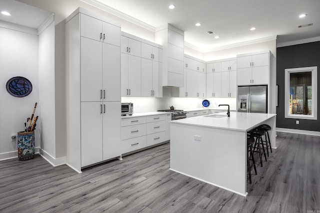 kitchen with white cabinetry, light hardwood / wood-style floors, a breakfast bar area, a center island with sink, and appliances with stainless steel finishes