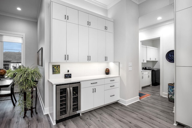 bar featuring ornamental molding, beverage cooler, white cabinets, washer / dryer, and light hardwood / wood-style floors