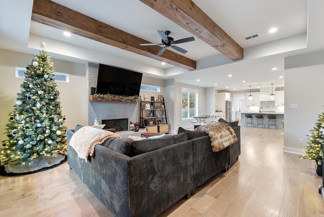 living room with sink, ceiling fan, light wood-type flooring, a fireplace, and beam ceiling