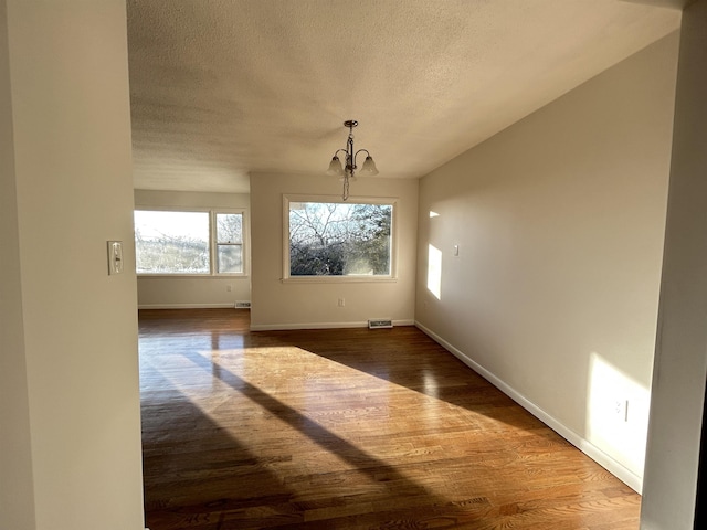 unfurnished dining area featuring a textured ceiling, dark wood-type flooring, and a notable chandelier