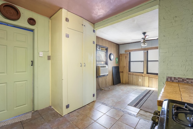 kitchen featuring tile counters, ceiling fan, stove, and wooden walls