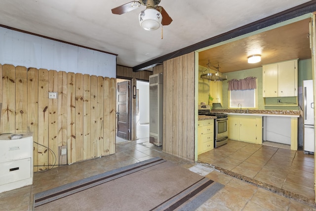 kitchen featuring gas range, ceiling fan, sink, white fridge, and wooden walls