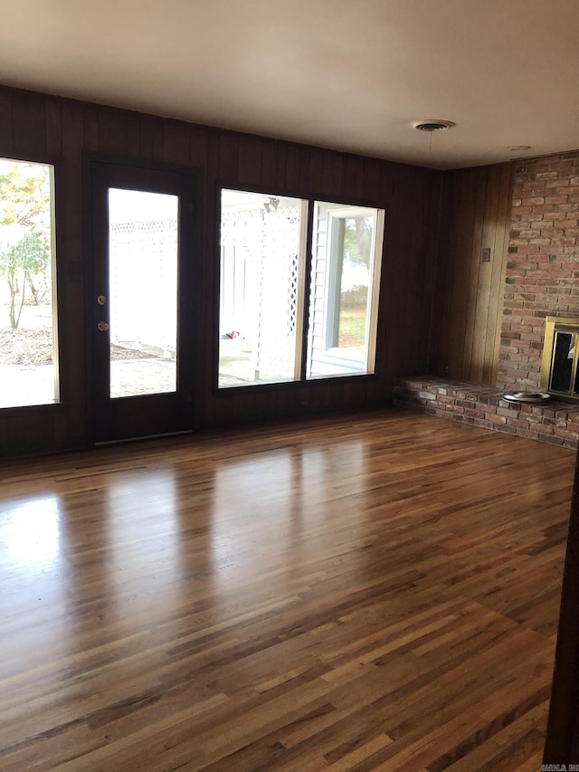 unfurnished living room with dark hardwood / wood-style flooring, a brick fireplace, and wood walls