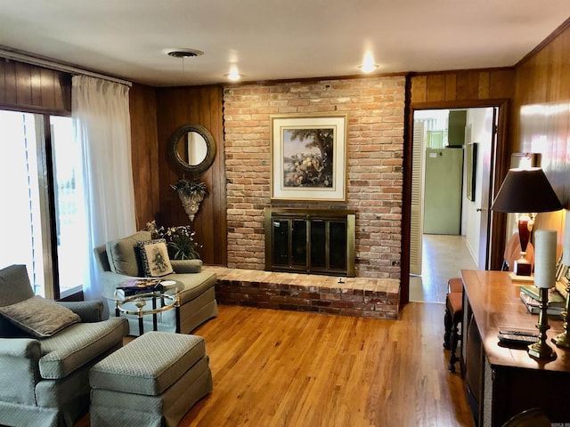 living room with a brick fireplace, light hardwood / wood-style flooring, and wood walls