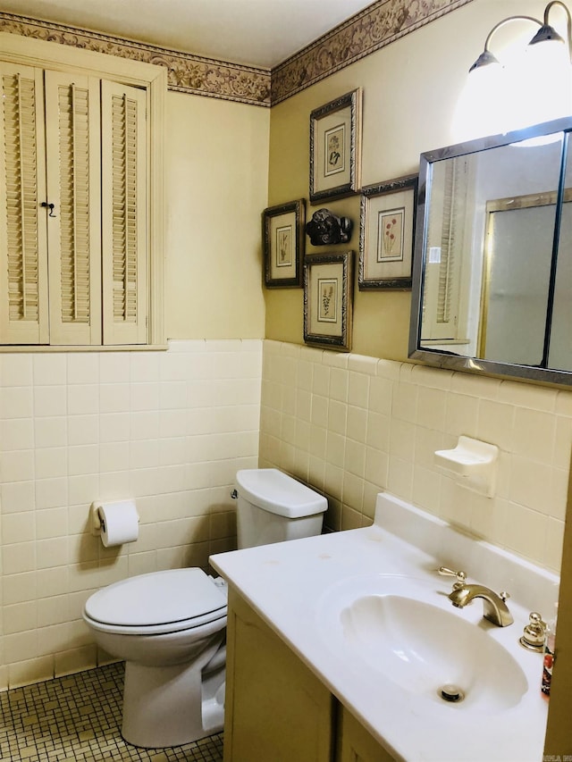 bathroom with toilet, vanity, tile patterned floors, and tile walls