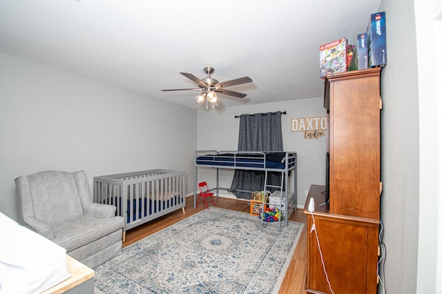 bedroom with hardwood / wood-style floors, ceiling fan, and a crib