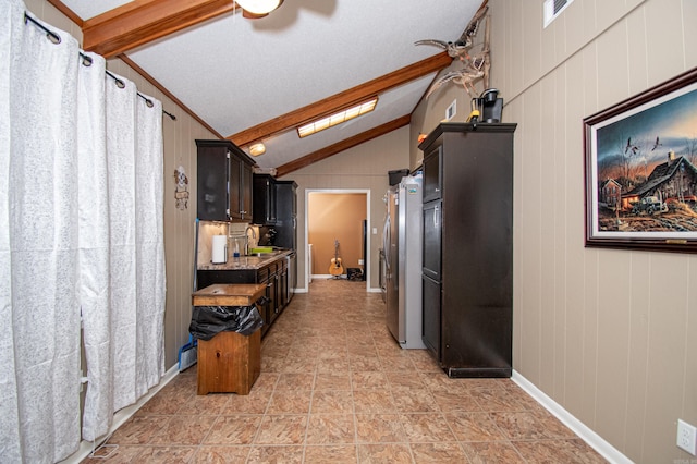 kitchen with sink, vaulted ceiling with beams, stainless steel fridge, wooden walls, and dark brown cabinets