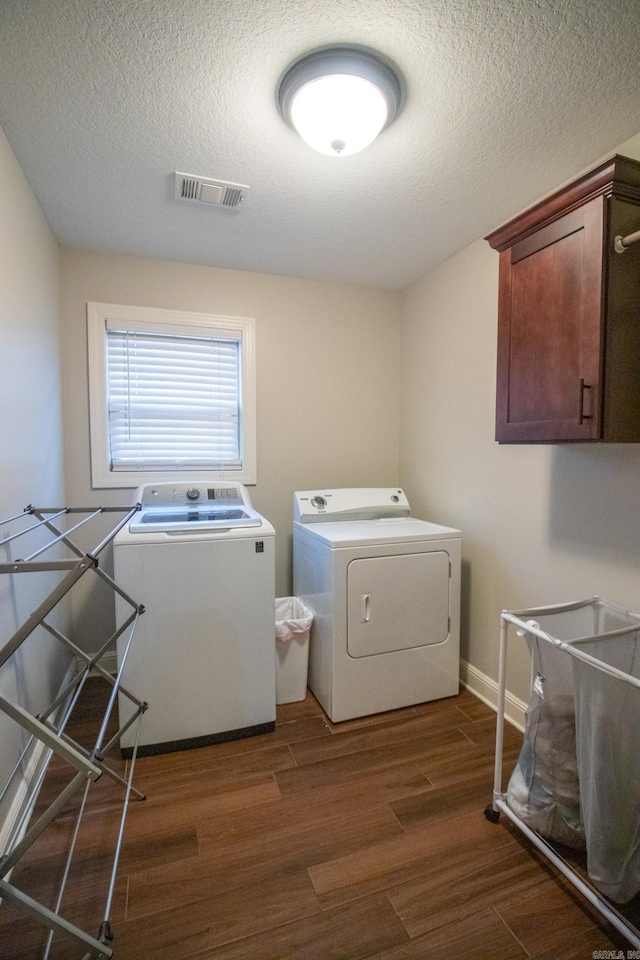 clothes washing area featuring washer and dryer, dark wood-type flooring, a textured ceiling, and cabinets