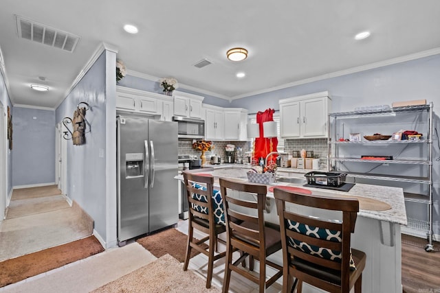 kitchen with backsplash, ornamental molding, appliances with stainless steel finishes, white cabinetry, and a breakfast bar area