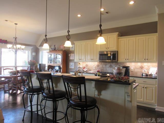 kitchen with crown molding, a center island with sink, a chandelier, and decorative light fixtures