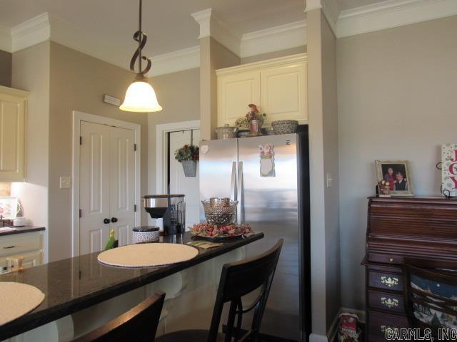 kitchen with white cabinets, stainless steel fridge, decorative light fixtures, and crown molding