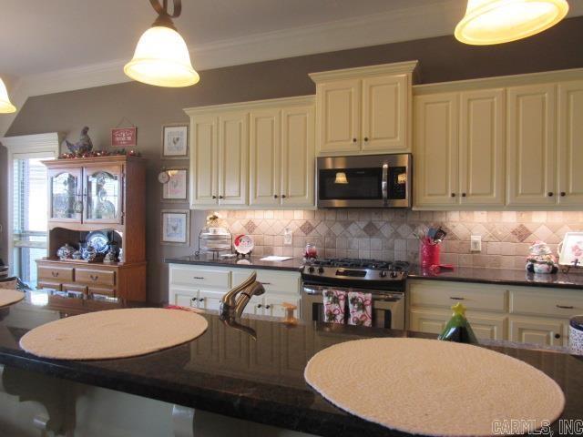 kitchen with decorative backsplash, appliances with stainless steel finishes, hanging light fixtures, and ornamental molding