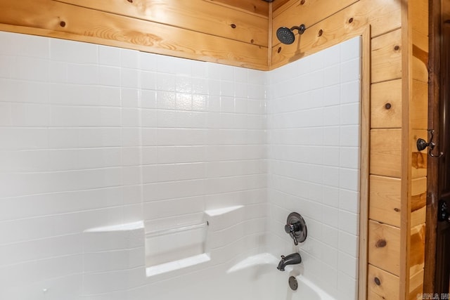 bathroom with tiled shower / bath combo and wooden walls