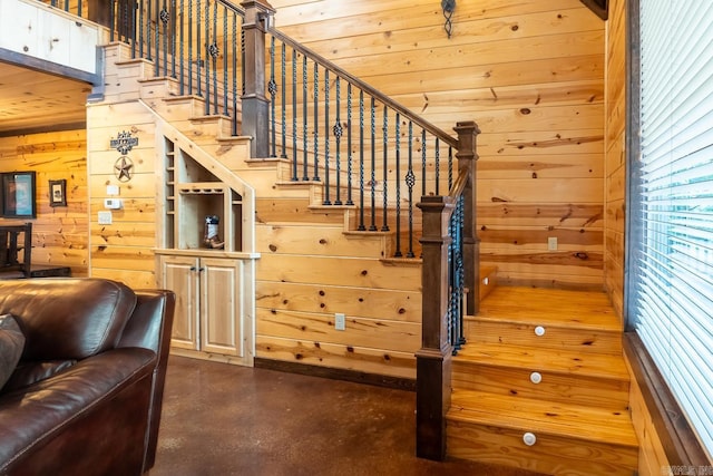 stairway with wood walls, concrete flooring, and wooden ceiling