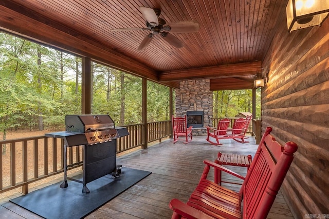 wooden deck featuring an outdoor stone fireplace, ceiling fan, and a grill