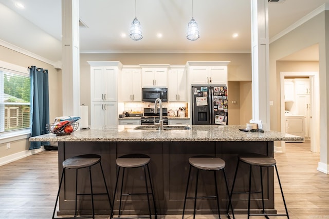 kitchen with light stone countertops, stainless steel appliances, sink, white cabinets, and light hardwood / wood-style floors