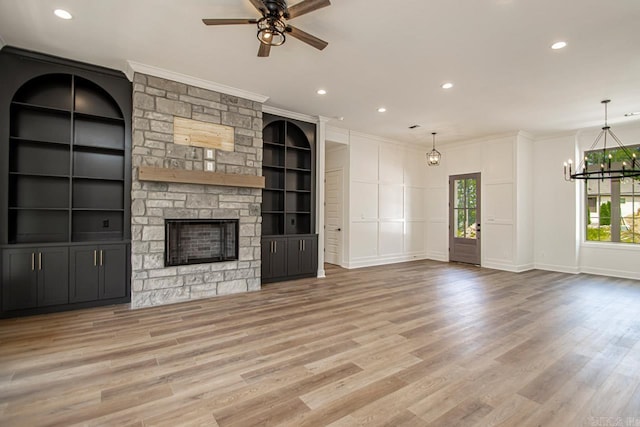 unfurnished living room with ceiling fan with notable chandelier, a stone fireplace, crown molding, and light hardwood / wood-style flooring