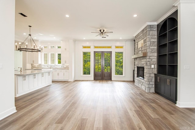 unfurnished living room with sink, light hardwood / wood-style floors, a fireplace, ceiling fan with notable chandelier, and ornamental molding