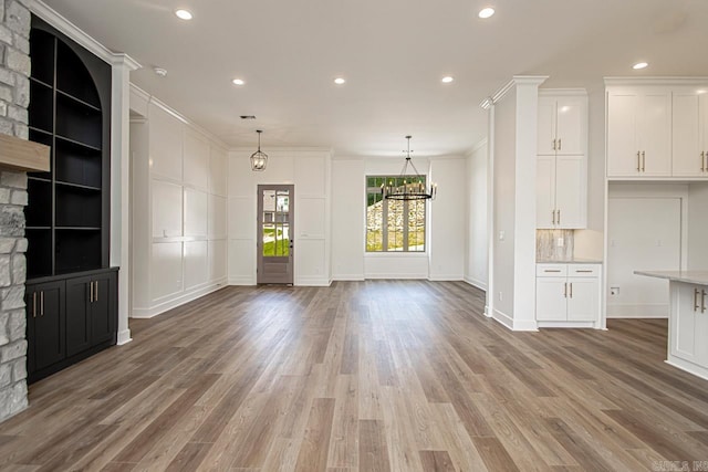 unfurnished living room featuring wood-type flooring, a stone fireplace, ornamental molding, and a notable chandelier