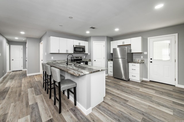 kitchen with kitchen peninsula, appliances with stainless steel finishes, dark stone countertops, white cabinets, and light hardwood / wood-style floors