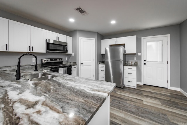 kitchen featuring sink, stainless steel appliances, dark hardwood / wood-style floors, dark stone countertops, and white cabinets