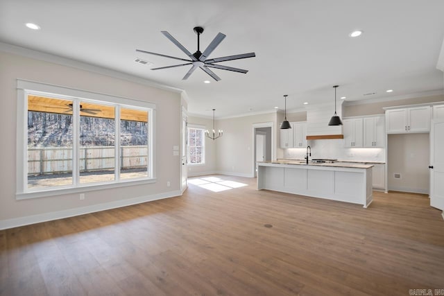 kitchen featuring crown molding, decorative light fixtures, a center island with sink, white cabinets, and light wood-type flooring