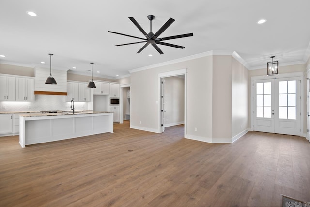 kitchen featuring a kitchen island with sink, white cabinets, hanging light fixtures, ornamental molding, and light hardwood / wood-style floors