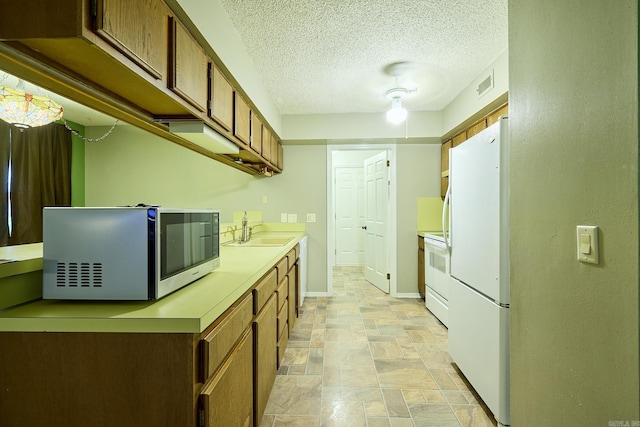 kitchen with a textured ceiling, white appliances, and sink