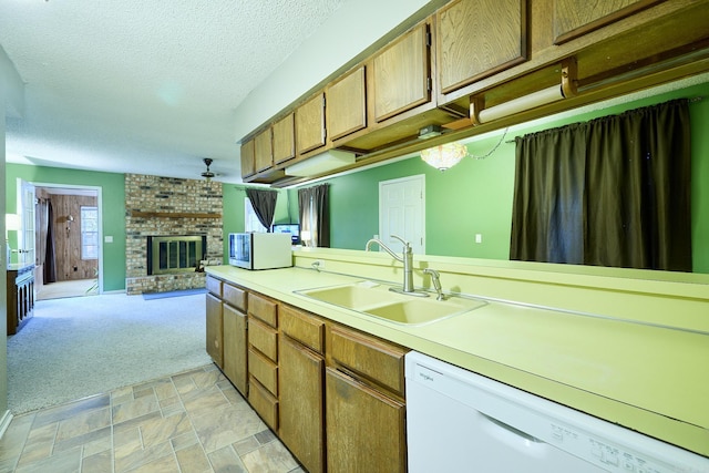 kitchen with a brick fireplace, a textured ceiling, white dishwasher, light colored carpet, and sink