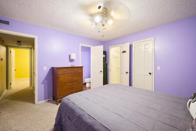 bedroom with ceiling fan, light colored carpet, a textured ceiling, and ensuite bath