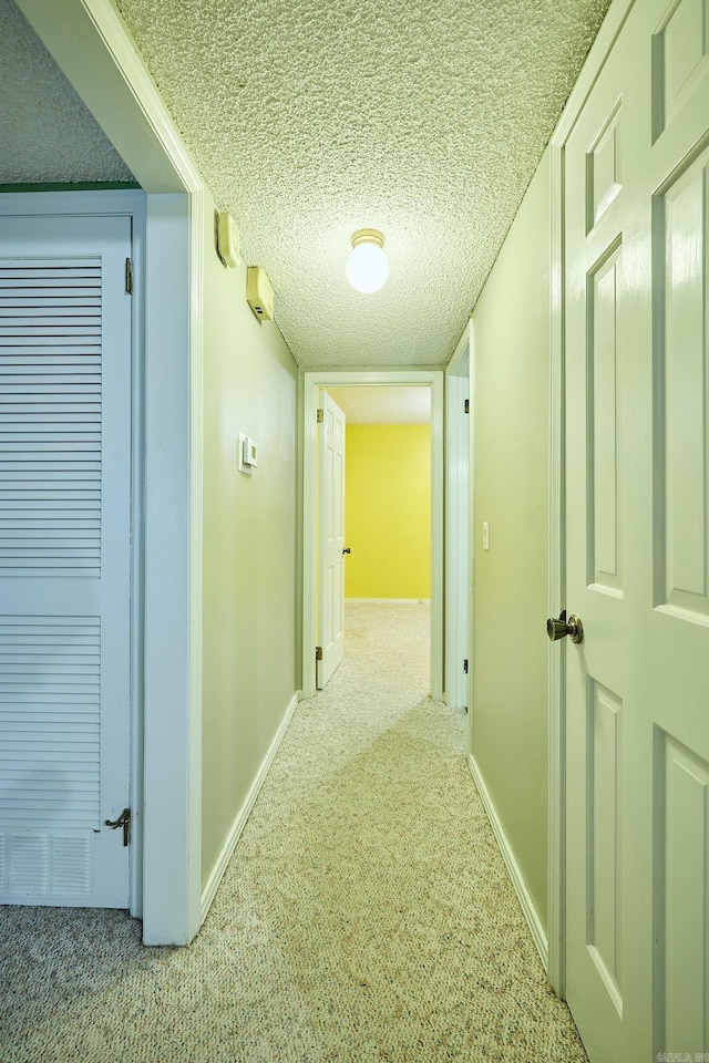 hall with a textured ceiling and light colored carpet