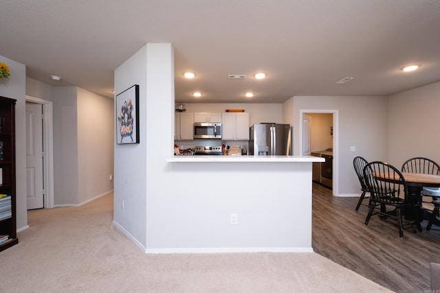 kitchen with light hardwood / wood-style floors, white cabinetry, kitchen peninsula, and appliances with stainless steel finishes