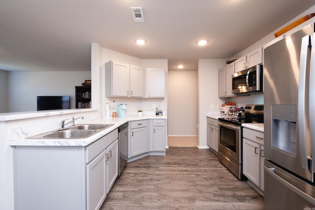 kitchen featuring kitchen peninsula, stainless steel appliances, sink, light hardwood / wood-style floors, and white cabinetry