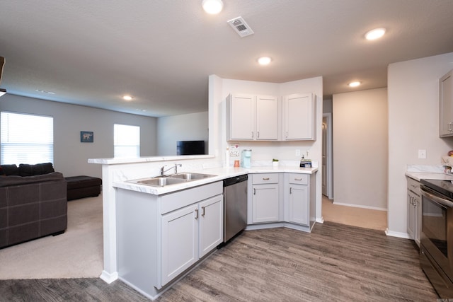 kitchen with white cabinetry, sink, stainless steel appliances, kitchen peninsula, and hardwood / wood-style flooring