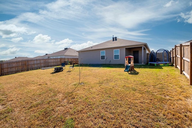 rear view of house featuring a trampoline and a lawn