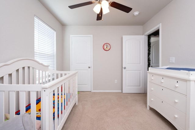 bedroom featuring light carpet, a nursery area, and ceiling fan