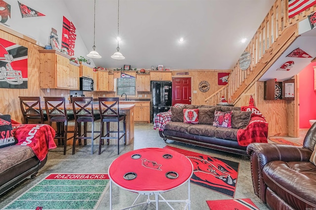 carpeted living room featuring wood walls, sink, and high vaulted ceiling