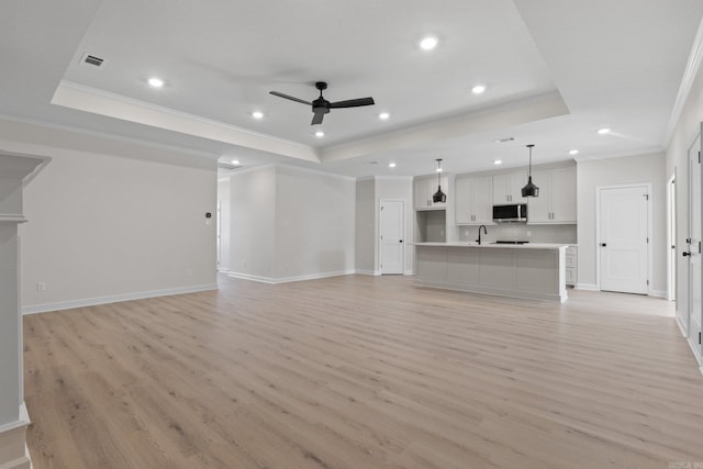 unfurnished living room featuring light hardwood / wood-style floors, a raised ceiling, and ceiling fan