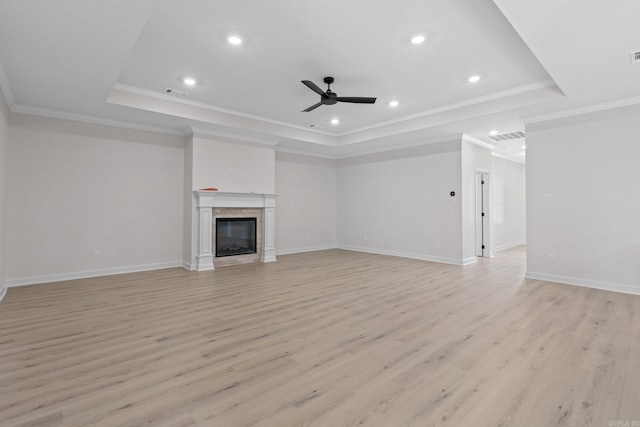 unfurnished living room featuring ceiling fan, a raised ceiling, a high end fireplace, crown molding, and light wood-type flooring