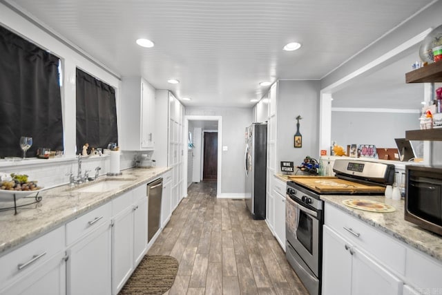 kitchen with light stone counters, stainless steel appliances, sink, hardwood / wood-style floors, and white cabinetry