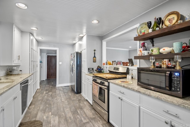 kitchen with sink, hardwood / wood-style flooring, appliances with stainless steel finishes, light stone counters, and white cabinetry