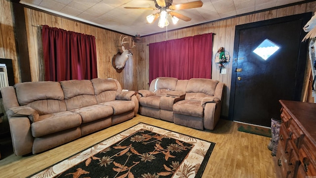 living room featuring ceiling fan, ornamental molding, wooden walls, and light hardwood / wood-style flooring