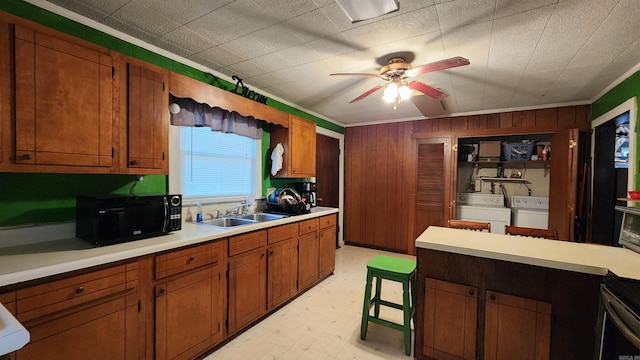 kitchen with wood walls, crown molding, sink, ceiling fan, and washing machine and dryer