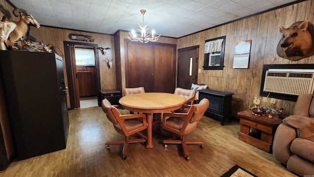 dining space featuring light wood-type flooring, ornamental molding, a wall mounted AC, an inviting chandelier, and wood walls