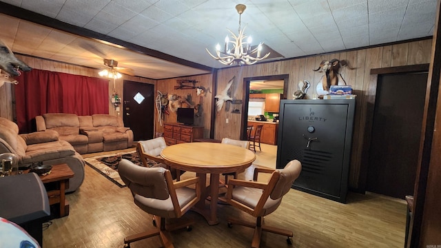 dining area with wood walls, light hardwood / wood-style floors, and ceiling fan with notable chandelier