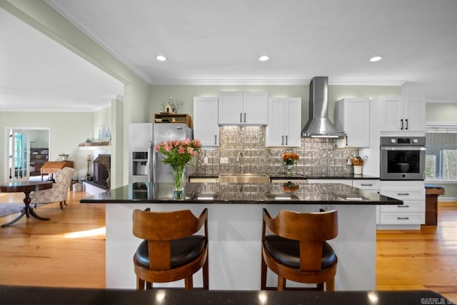 kitchen with white cabinets, stainless steel appliances, light hardwood / wood-style floors, and wall chimney range hood