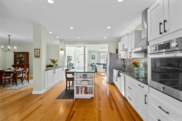 kitchen featuring pendant lighting, wall chimney range hood, light hardwood / wood-style floors, white cabinetry, and stainless steel appliances